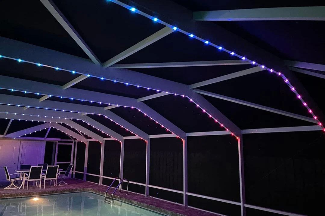 Attached image file A screened-in patio with a pool features LED strip lights overhead glowing in blue, purple, and red. Patio furniture is arranged near the pool against the far wall.