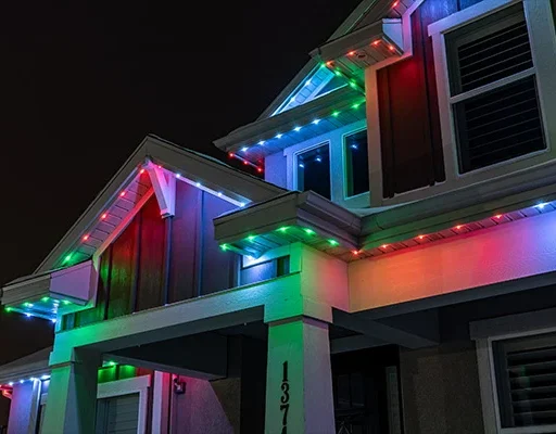 Attached image file A house at night with colorful LED lights in red, blue, green, and white outlining the roof and eaves, creating a festive appearance. The house number 137 is visible on a white pillar.