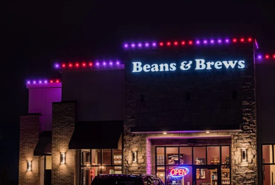 Attached image file A Beans & Brews coffee shop at night, with purple and red lights along the roof and a bright OPEN neon sign in the window.